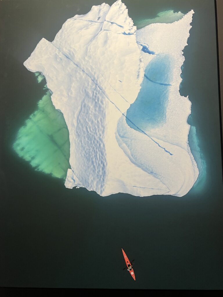 Iceberg e canoista in una fotografia della mostra Oceani di ghiaccio, mari d’oro al Galata Museo del Mare di Genova.
